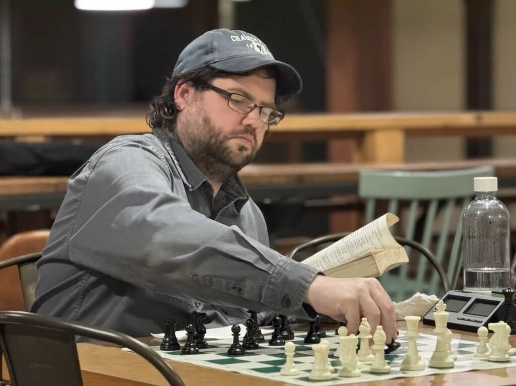 Club organizer, Mike Terrill, sitting at a table in front of a chess board studying a game with book in hand.